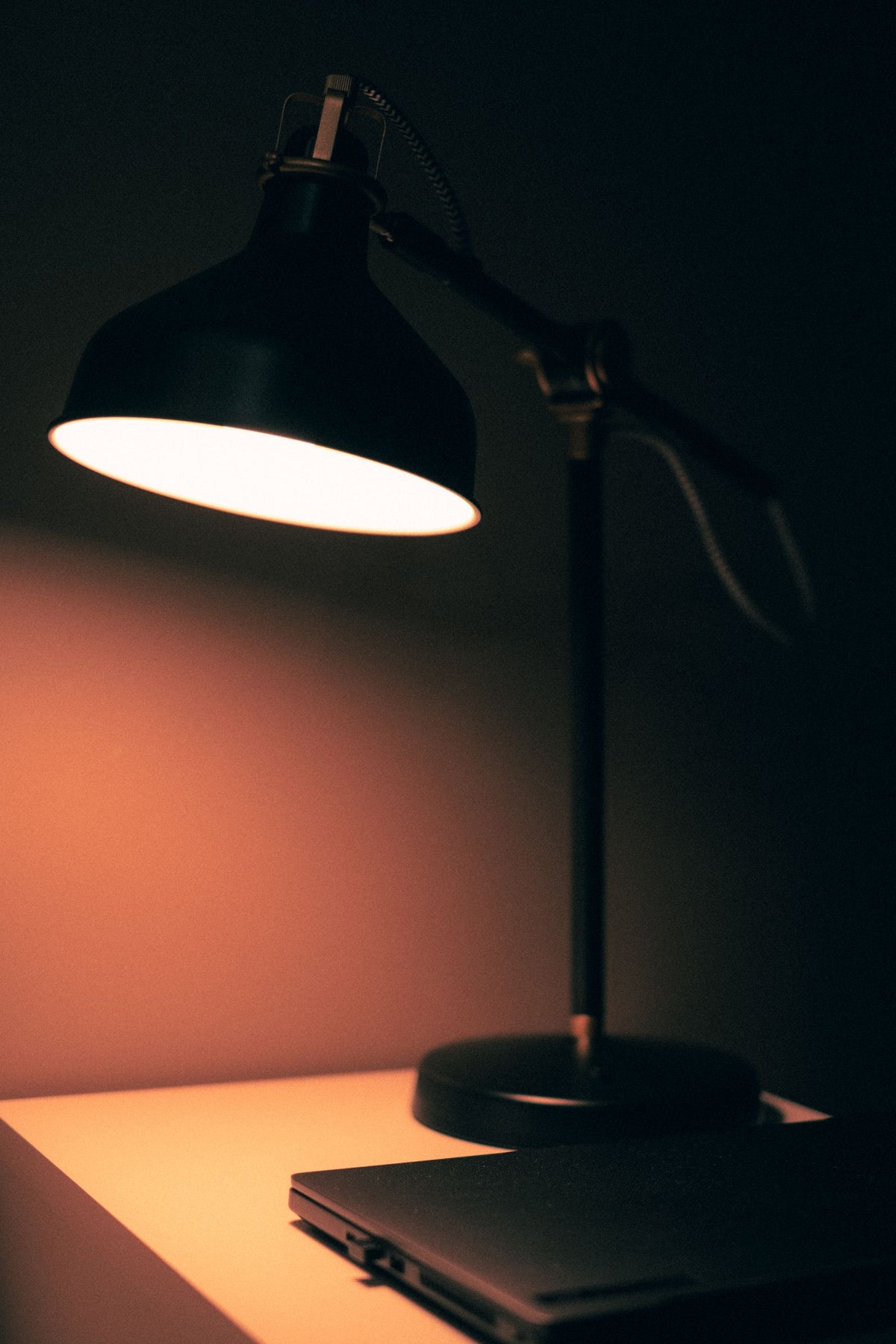Black desk lamp glowing warm white on a dark desk