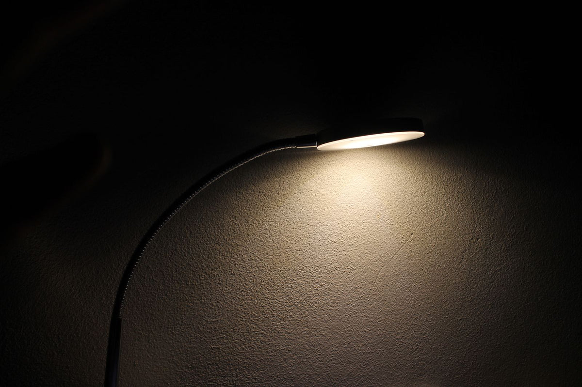 Detail of a desk lamp head casting warm light across a dark desk