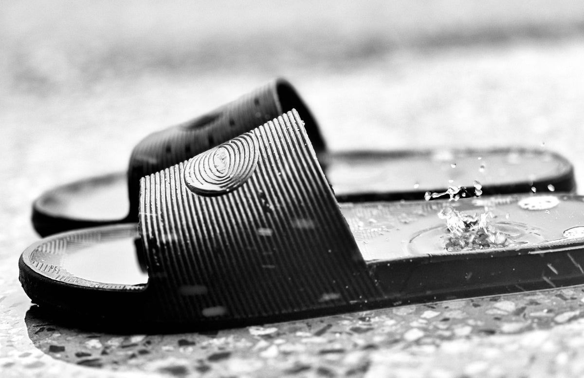 Everyday Slide in Black — black moulded slide sandal with one wide strap, close-up on a wet surface
