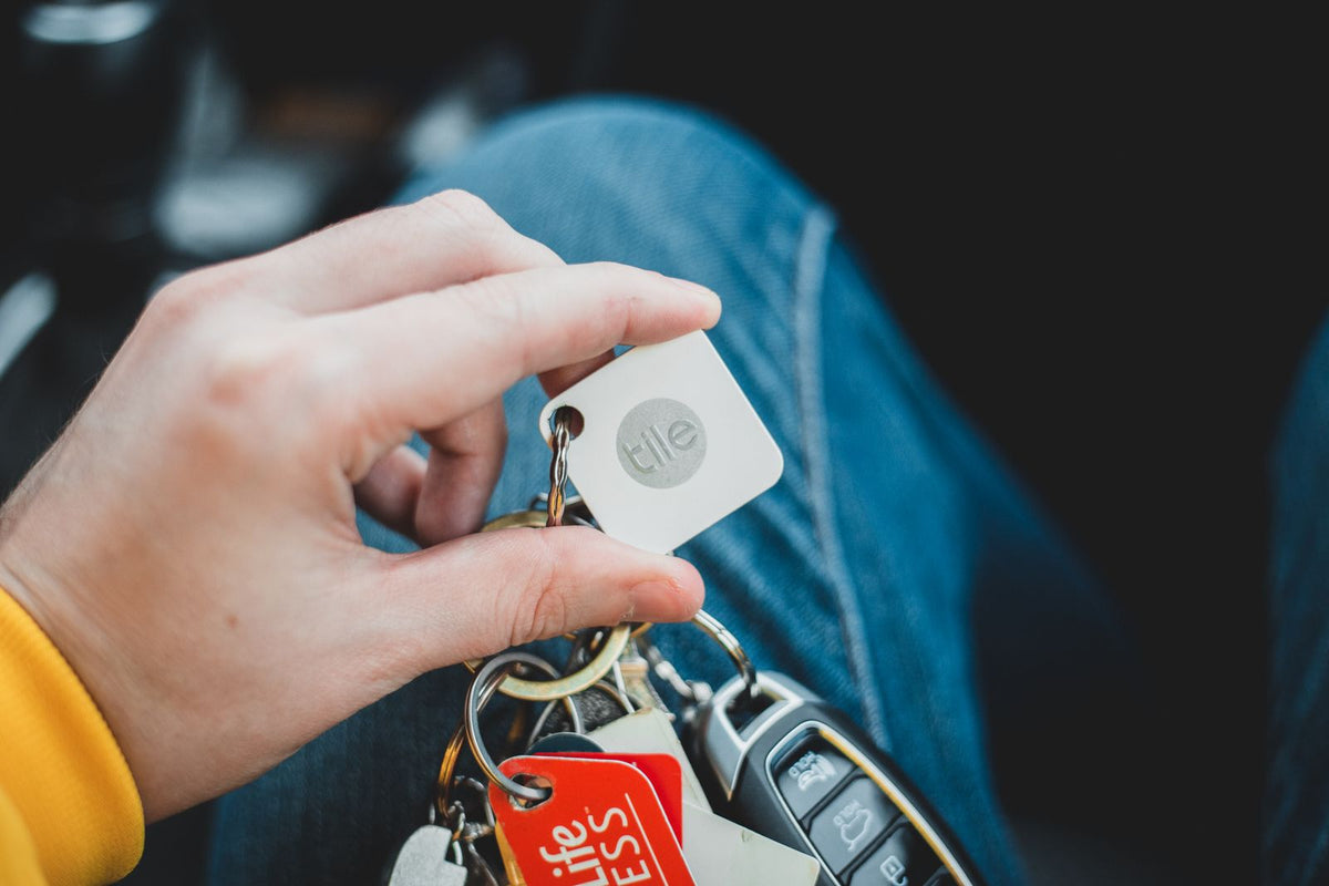 Small white item tracker attached to a key ring, held in a hand