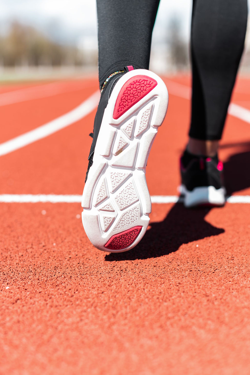 Road Tempo — runner on a track seen from behind, close-up of the running shoe outsole and stacked midsole