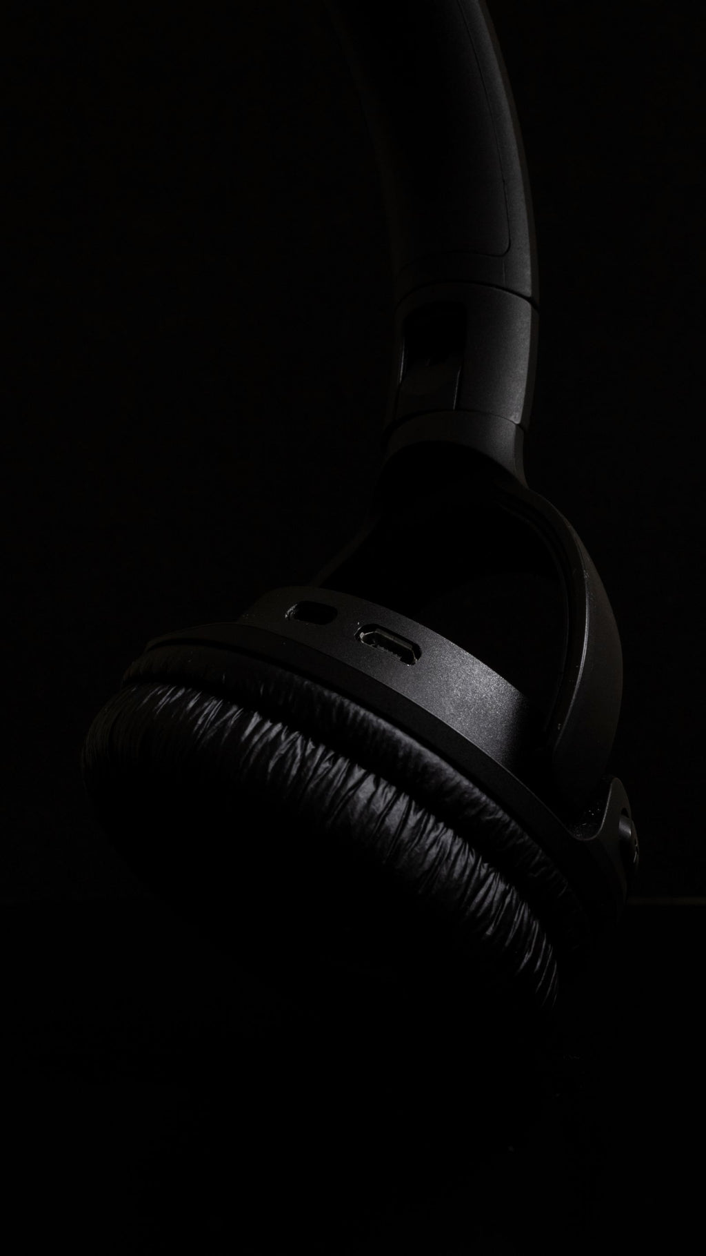 Close-up of a black over-ear headphone ear cup and hinge in low light