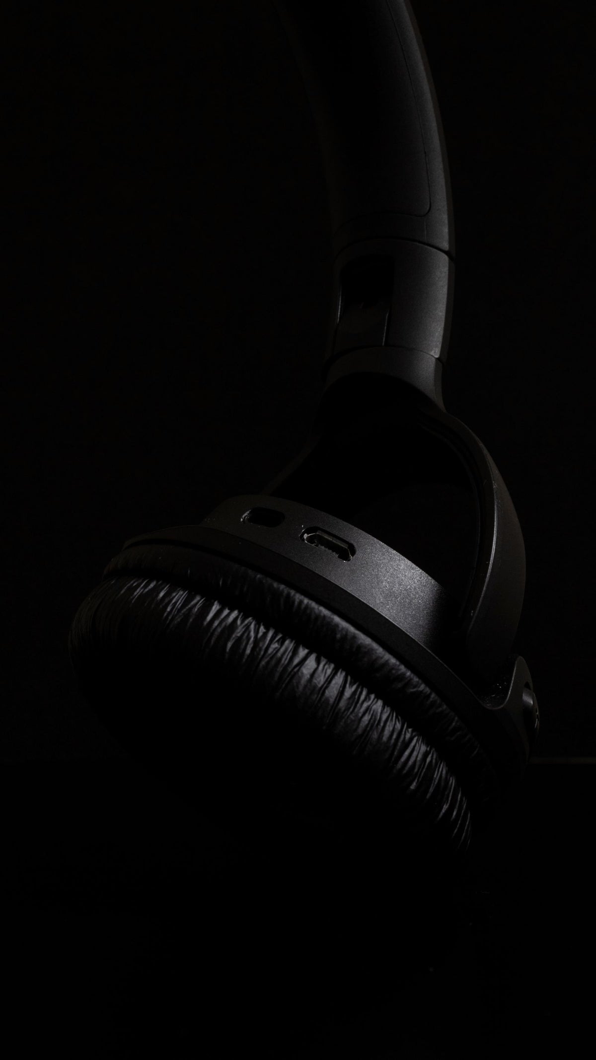 Close-up of a black over-ear headphone ear cup and hinge in low light