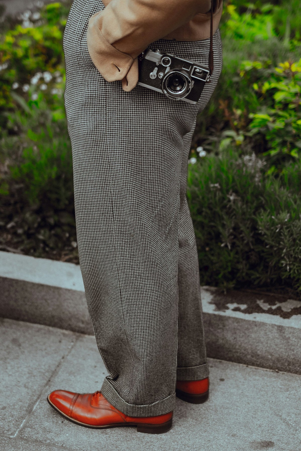 Man wearing grey wool trousers with a camera on a city pavement