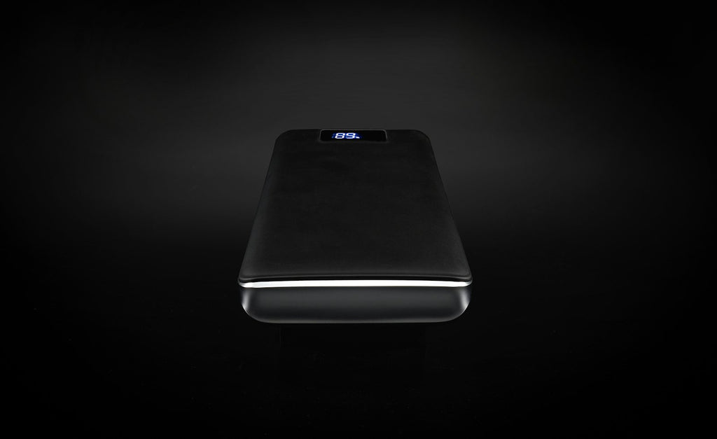 Slim black power bank with its charge indicator lit, on a black backdrop