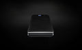 Slim black power bank with its charge indicator lit, on a black backdrop