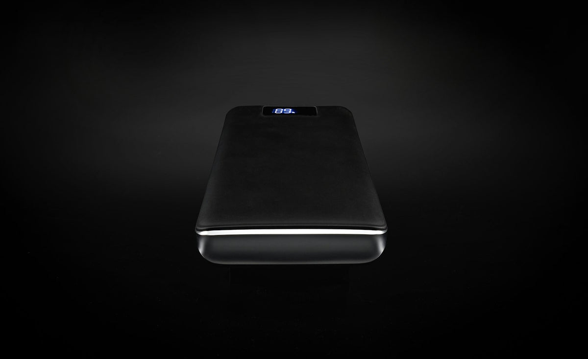 Slim black power bank with its charge indicator lit, on a black backdrop