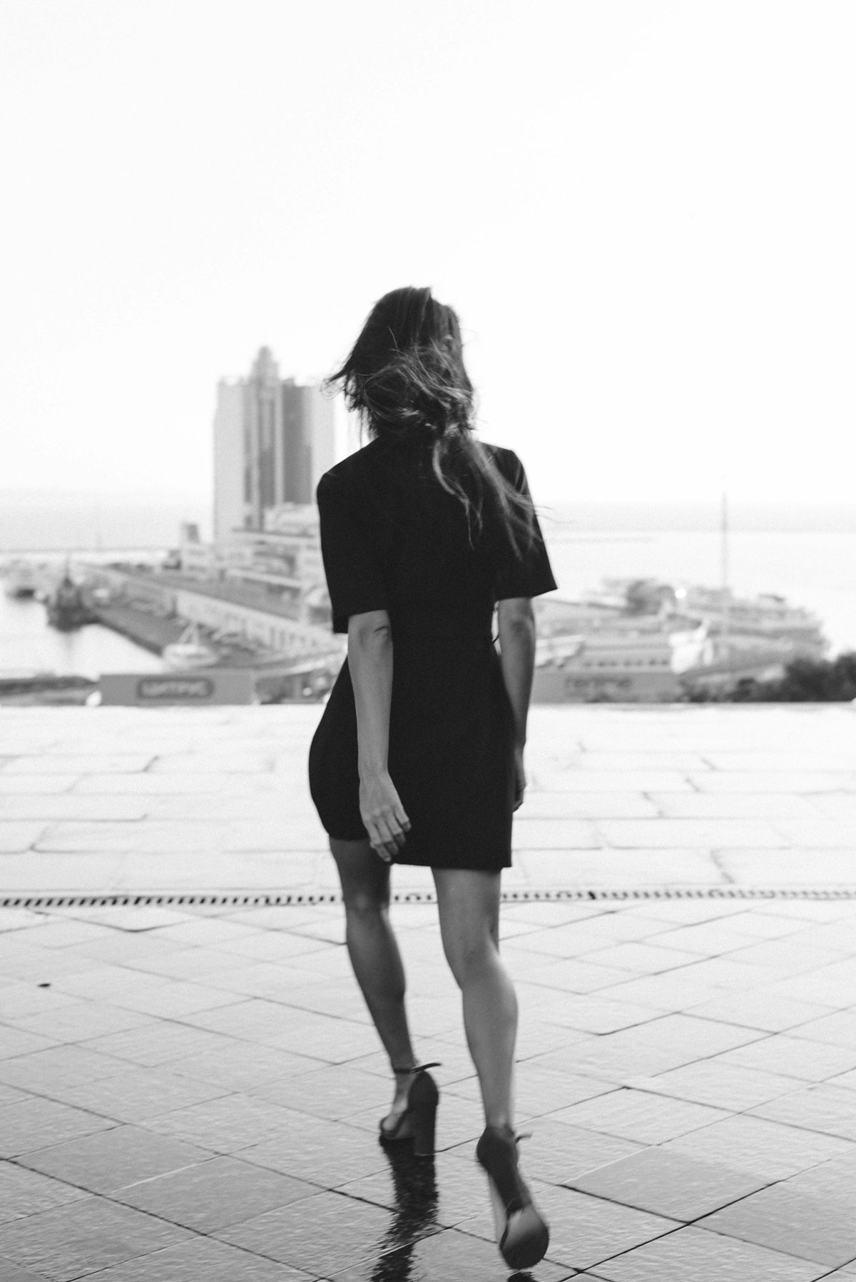 Woman in a black dress walking along a city waterfront