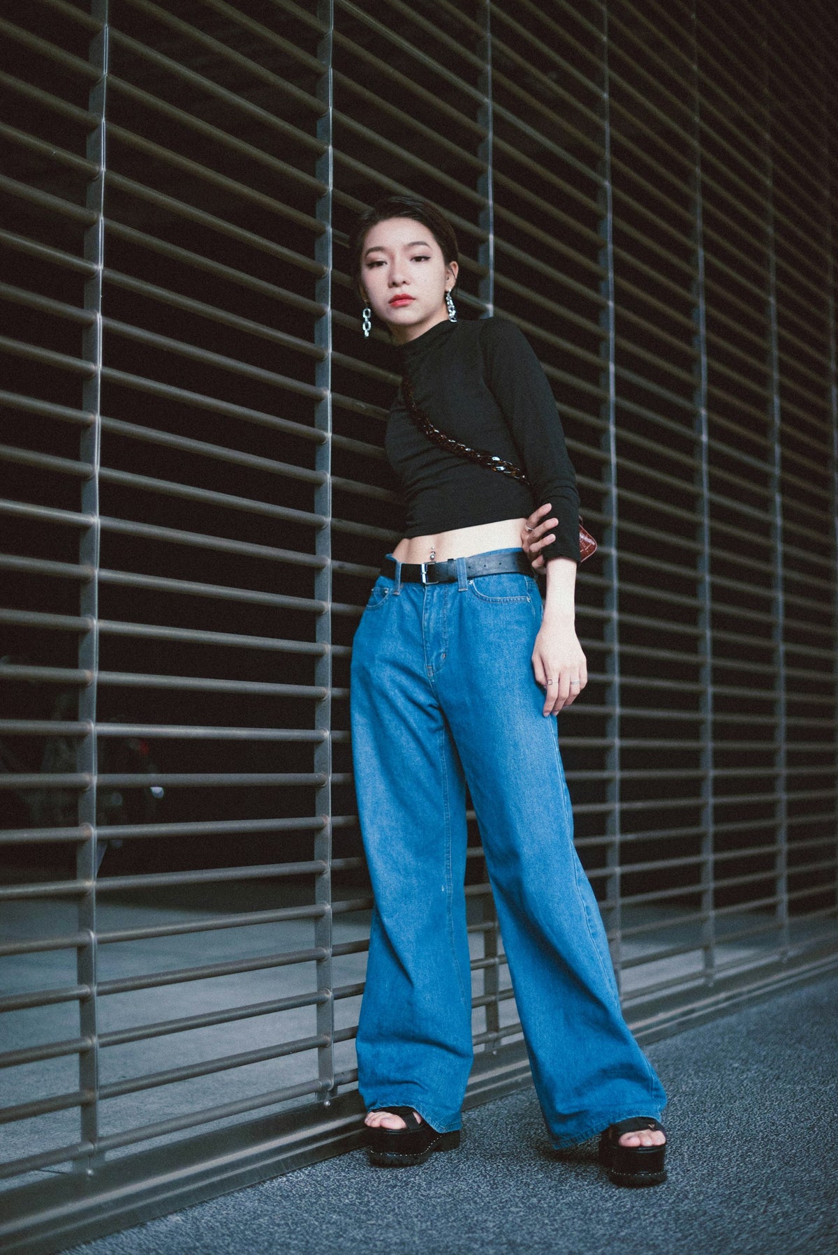 Woman wearing wide-leg blue jeans with a black top, standing beside a metal roll-up door