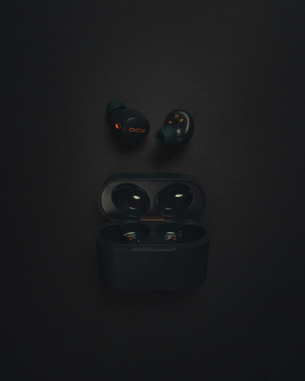 Wireless earbuds beside their open charging case on a dark surface
