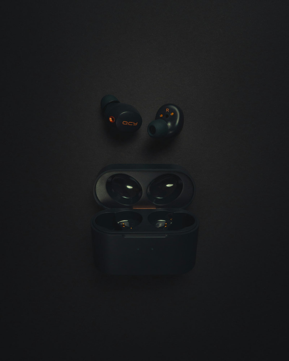 Wireless earbuds beside their open charging case on a dark surface