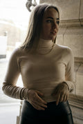 Woman wearing an oat-coloured turtleneck sweater beside a stone facade, natural light