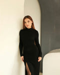 Woman in a long-sleeved black column dress leaning against a warm neutral wall