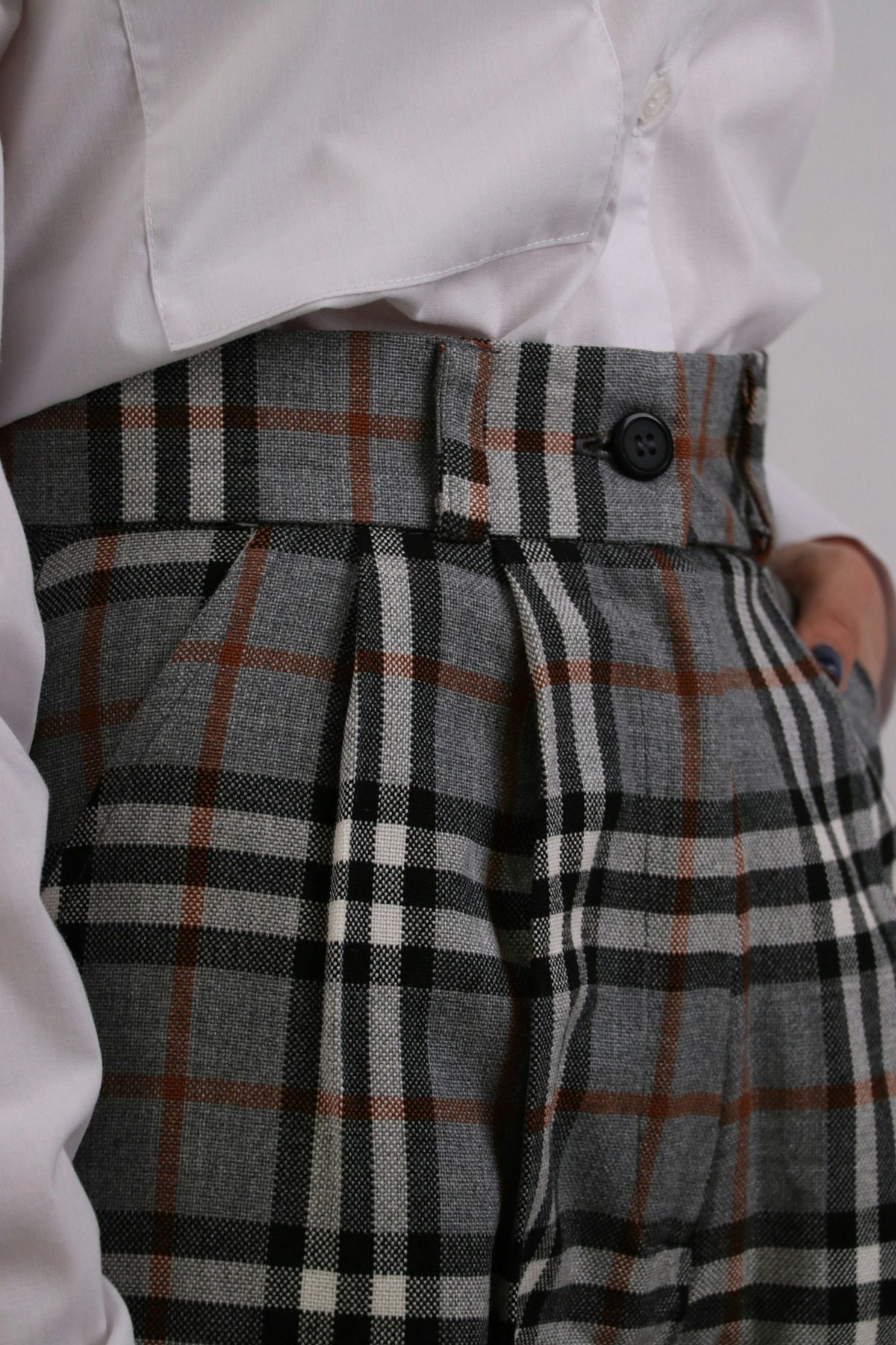 Close-up of the pleated waistband of checked wool trousers with a tucked white shirt