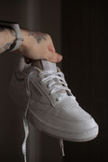 White Stitched Low Top — Photographic Demo — photograph 1. Photo: @felirbe; https://unsplash.com/photos/a-person-holding-a-pair-of-white-sneakers-7RhUBg1QROk. Photographic demo.